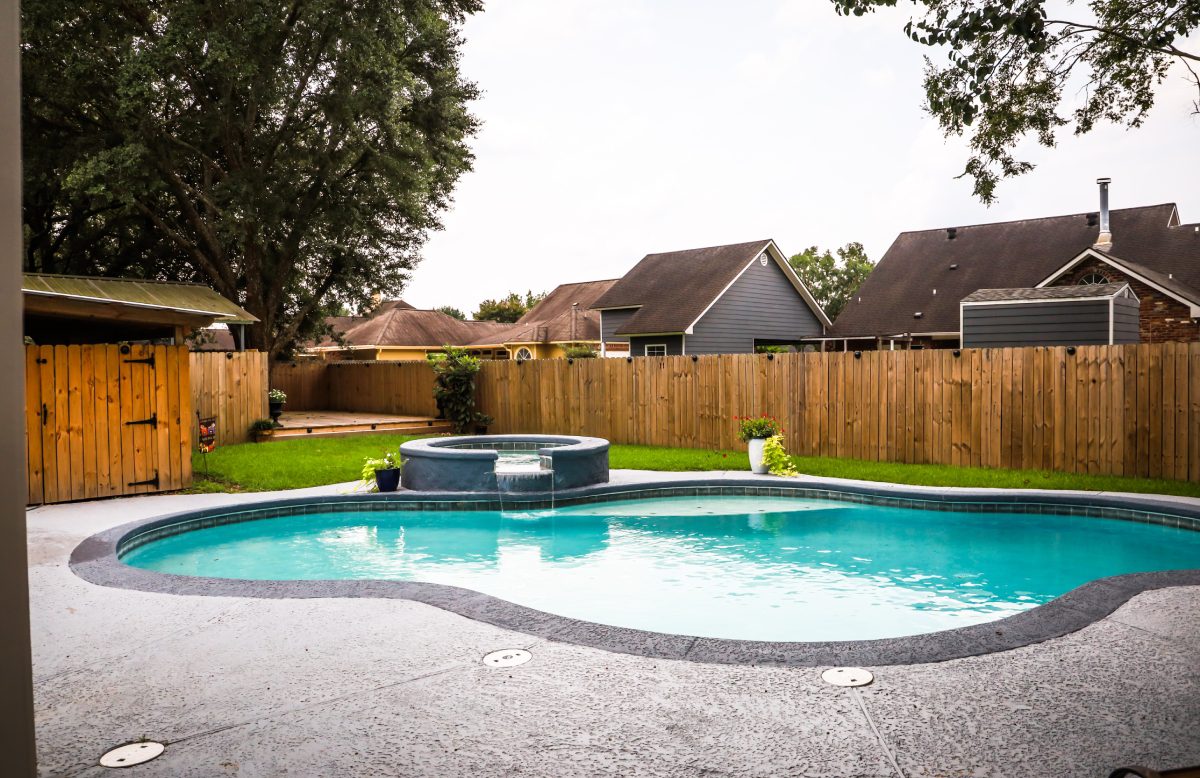 Backyard pool with wooden fence and trees.