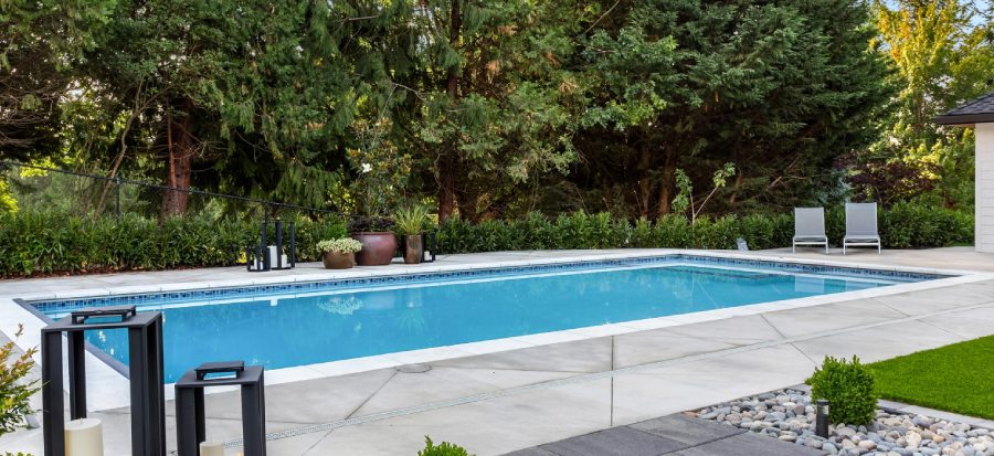 Backyard pool surrounded by trees and chairs.