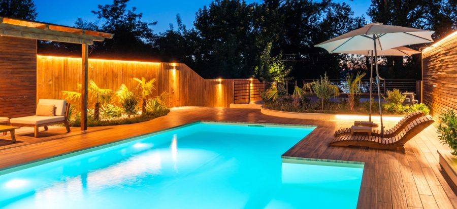 Modern backyard pool with deck and lighting.